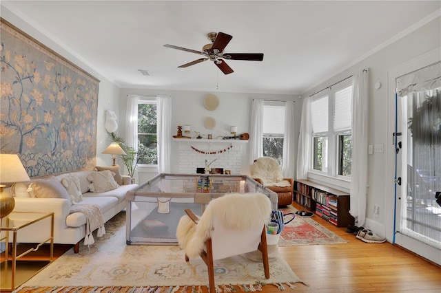 living room featuring crown molding, a brick fireplace, plenty of natural light, and light wood-type flooring