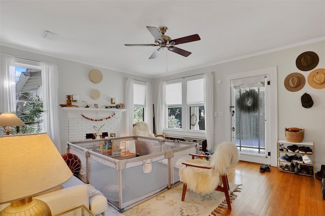 interior space with ornamental molding, a brick fireplace, ceiling fan, and light hardwood / wood-style floors