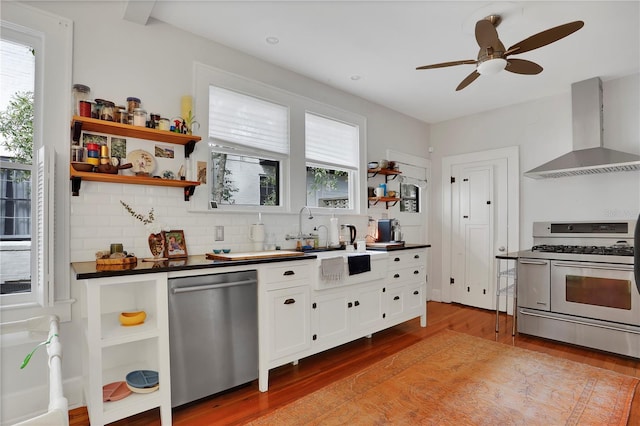 kitchen featuring wall chimney exhaust hood, white cabinetry, light hardwood / wood-style flooring, stainless steel appliances, and decorative backsplash