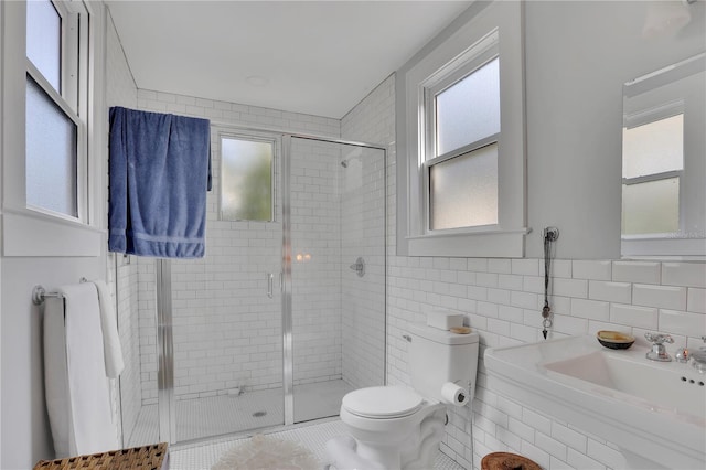 bathroom with sink, toilet, a shower with door, and tile walls