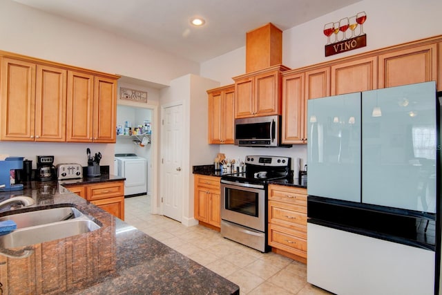 kitchen featuring sink, light tile patterned floors, stainless steel appliances, washer and dryer, and dark stone counters