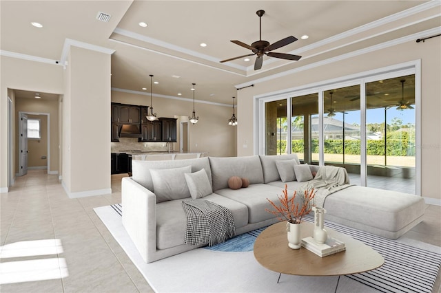 tiled living room with ceiling fan, ornamental molding, and a raised ceiling