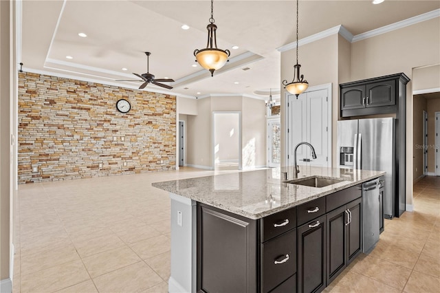 kitchen featuring an island with sink, a tray ceiling, sink, and hanging light fixtures