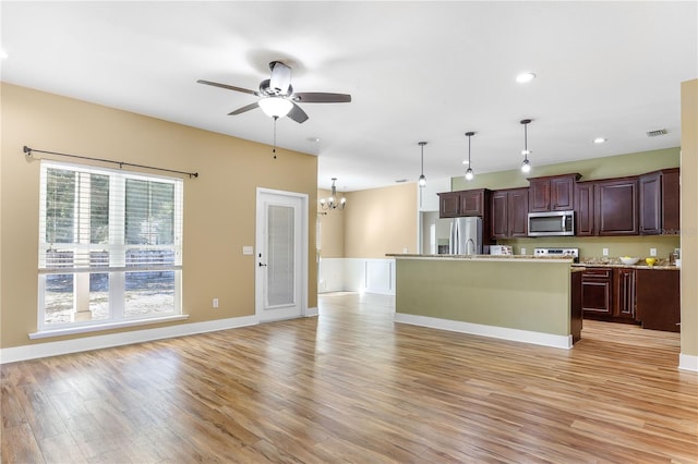 kitchen with hanging light fixtures, light wood-type flooring, a kitchen island with sink, stainless steel appliances, and ceiling fan with notable chandelier