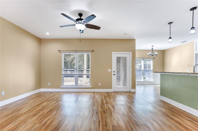 spare room featuring plenty of natural light, ceiling fan with notable chandelier, and light hardwood / wood-style flooring