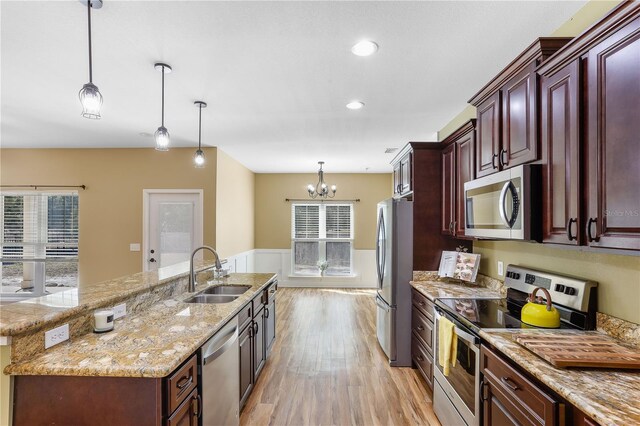 kitchen featuring sink, hanging light fixtures, appliances with stainless steel finishes, an island with sink, and light hardwood / wood-style floors