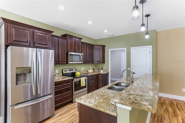 kitchen with sink, light hardwood / wood-style flooring, appliances with stainless steel finishes, an island with sink, and pendant lighting