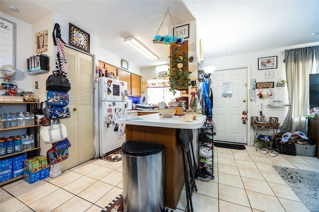 kitchen with light tile patterned floors, a breakfast bar area, kitchen peninsula, and white refrigerator