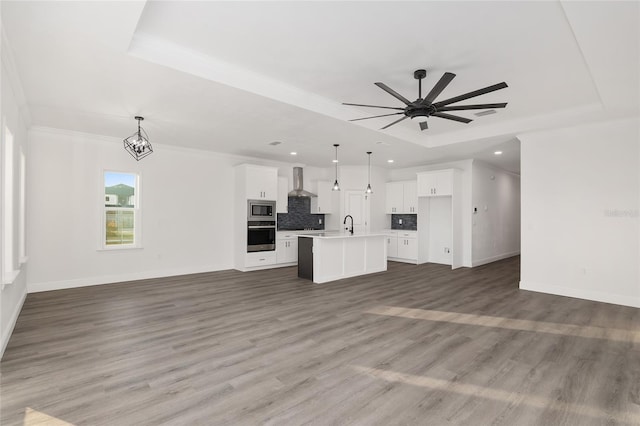 unfurnished living room with sink, ornamental molding, dark hardwood / wood-style floors, a raised ceiling, and ceiling fan with notable chandelier