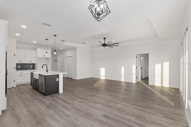 kitchen with white cabinetry, a tray ceiling, hanging light fixtures, and a center island with sink