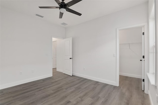 unfurnished bedroom with hardwood / wood-style flooring, a walk in closet, ceiling fan, and a closet