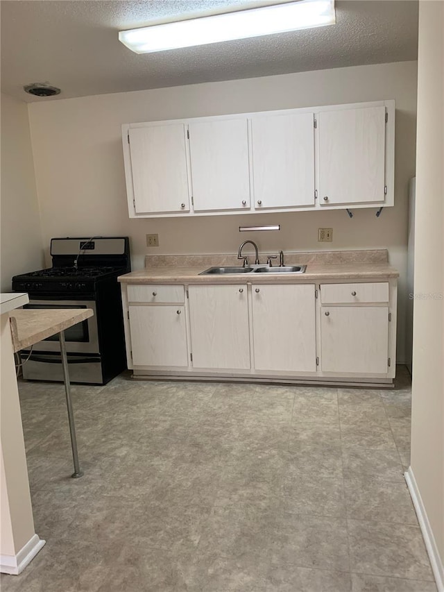 kitchen featuring stainless steel gas stove, sink, white cabinetry, and a textured ceiling