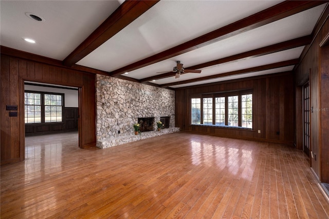 unfurnished living room with beamed ceiling, a stone fireplace, wooden walls, and light wood-type flooring