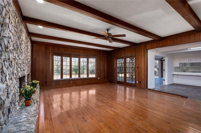 unfurnished living room with hardwood / wood-style floors, beamed ceiling, a textured ceiling, and wood walls