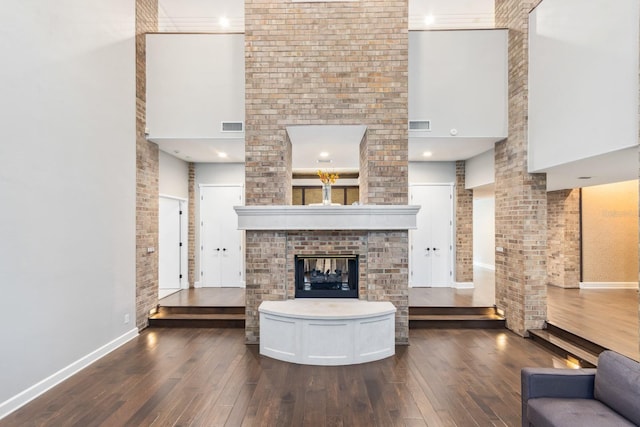 unfurnished living room featuring a brick fireplace, a towering ceiling, and dark hardwood / wood-style flooring