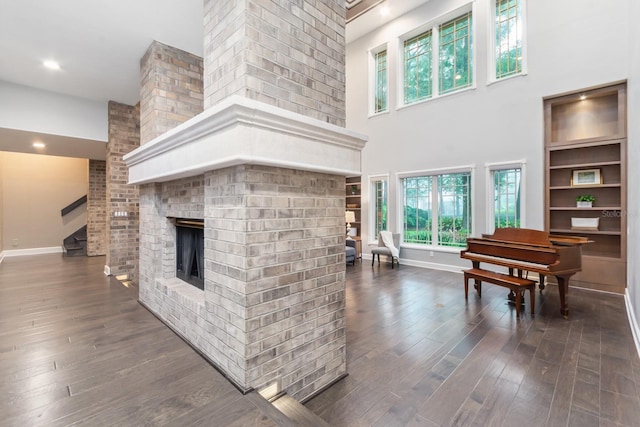 living room with a brick fireplace, built in shelves, dark hardwood / wood-style floors, and a high ceiling