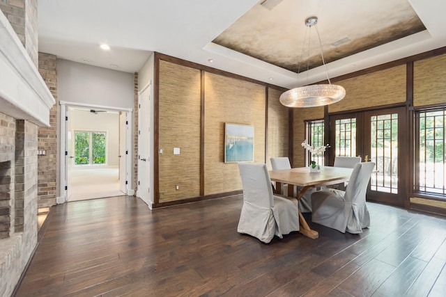 dining space featuring a brick fireplace, a tray ceiling, dark wood-type flooring, and french doors