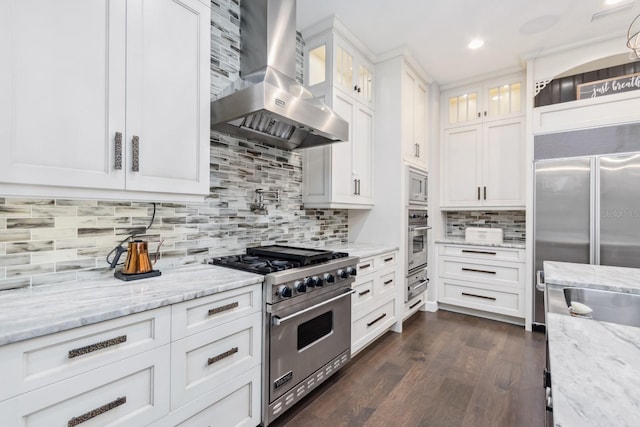 kitchen with white cabinetry, built in appliances, dark hardwood / wood-style floors, light stone countertops, and wall chimney range hood