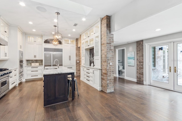 kitchen with french doors, a breakfast bar area, built in appliances, decorative light fixtures, and a kitchen island with sink