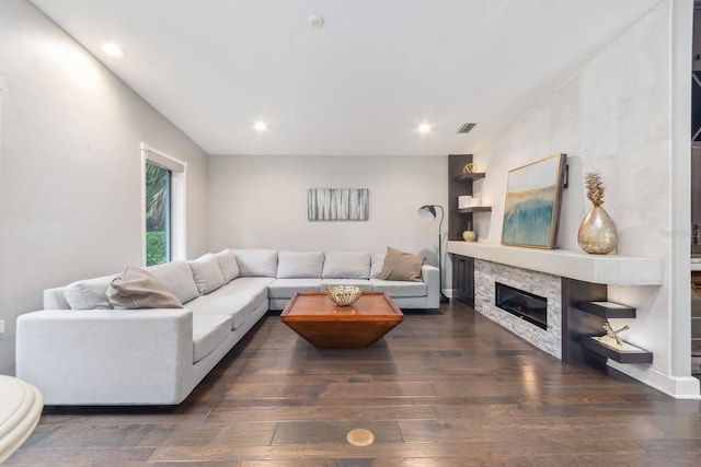 living room featuring a stone fireplace and dark wood-type flooring