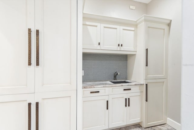 bar featuring light stone countertops, sink, decorative backsplash, and white cabinets