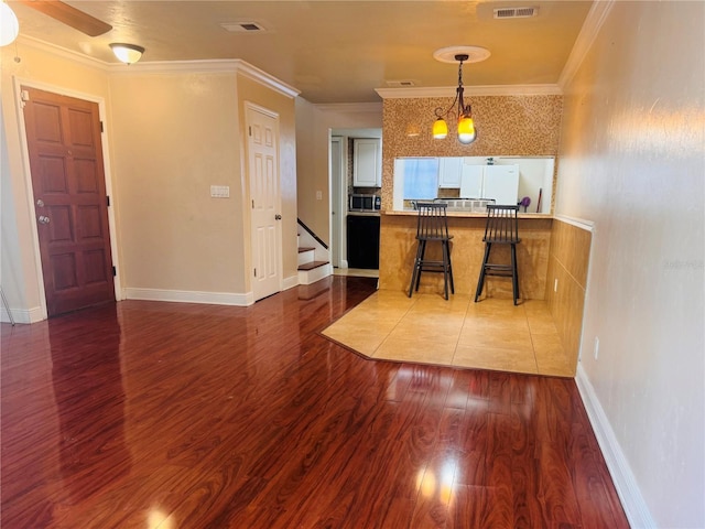 kitchen with dark wood-type flooring, white refrigerator, ornamental molding, a kitchen breakfast bar, and kitchen peninsula