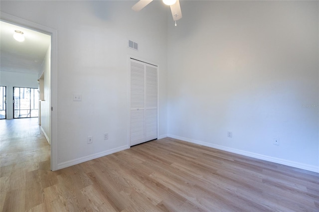 unfurnished bedroom with a towering ceiling, light hardwood / wood-style flooring, a closet, and ceiling fan