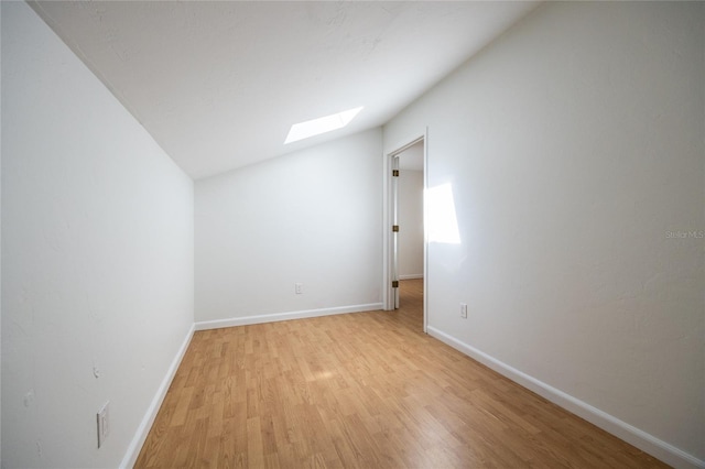 empty room featuring lofted ceiling with skylight and light hardwood / wood-style floors