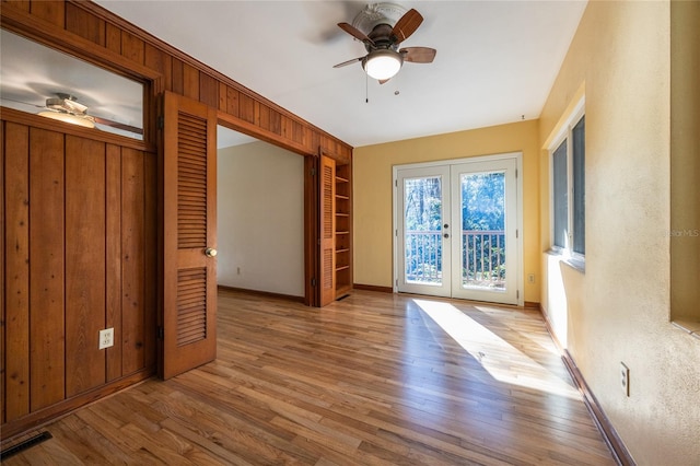 interior space with ceiling fan, wooden walls, light wood-type flooring, and french doors