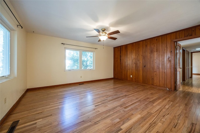 spare room with ceiling fan, light hardwood / wood-style flooring, and wood walls