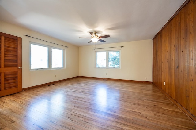 empty room with ceiling fan, wood walls, and light wood-type flooring