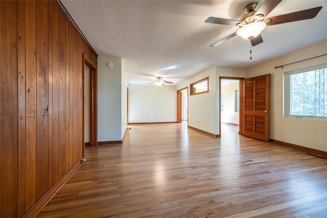 empty room with ceiling fan, wooden walls, and light hardwood / wood-style flooring