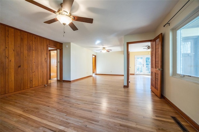 unfurnished room featuring wooden walls, ceiling fan, and light wood-type flooring