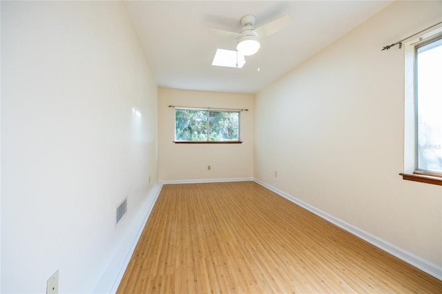 spare room with light hardwood / wood-style flooring, ceiling fan, and a skylight