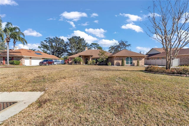 ranch-style house featuring a front lawn, a chimney, fence, and brick siding