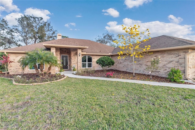 ranch-style home featuring a chimney, brick siding, roof with shingles, and a front yard