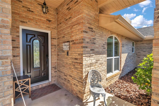 doorway to property with a shingled roof and brick siding