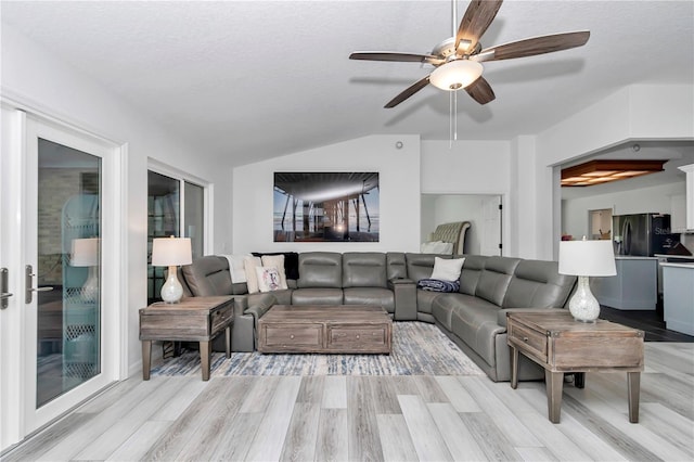 living area with lofted ceiling, a textured ceiling, light wood-style flooring, and a ceiling fan