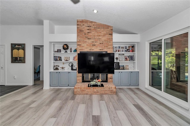 living area with a textured ceiling, lofted ceiling, built in shelves, baseboards, and light wood finished floors