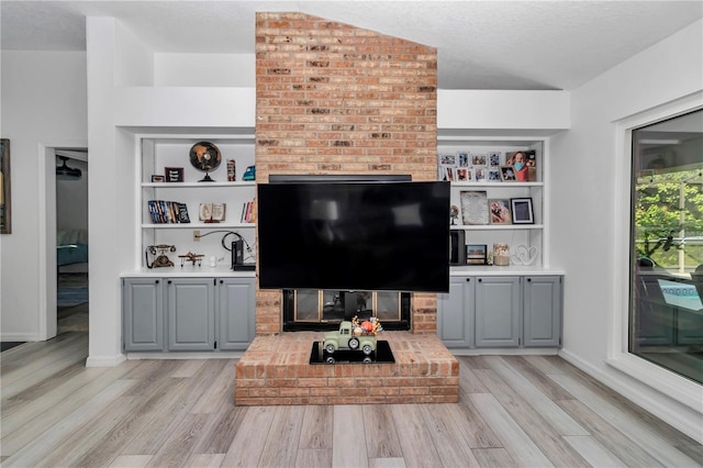 living room with light wood finished floors, baseboards, a textured ceiling, a brick fireplace, and built in shelves