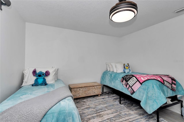 bedroom with a textured ceiling, wood finished floors, and visible vents