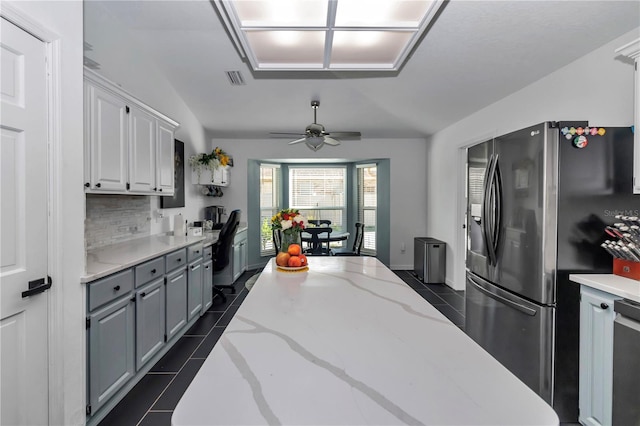 kitchen with stainless steel fridge, dark tile patterned flooring, light stone countertops, vaulted ceiling, and backsplash