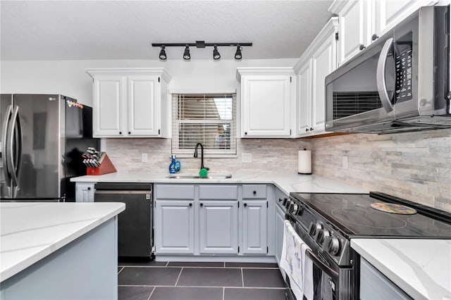 kitchen with stainless steel appliances, backsplash, white cabinetry, a sink, and light stone countertops