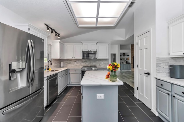 kitchen with white cabinets, light stone counters, a center island, stainless steel appliances, and a sink