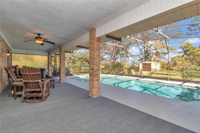 outdoor pool with glass enclosure, a patio area, and a ceiling fan