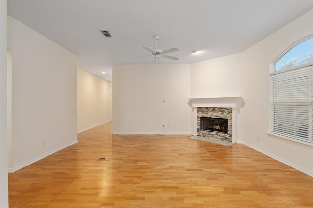 unfurnished living room featuring a stone fireplace, ceiling fan, and light hardwood / wood-style flooring