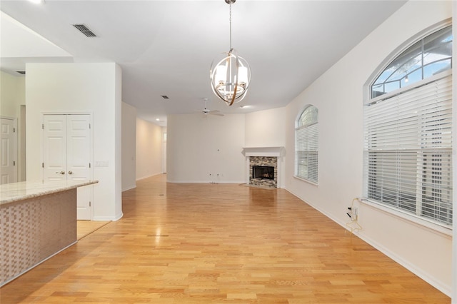 unfurnished living room with ceiling fan with notable chandelier and light hardwood / wood-style flooring