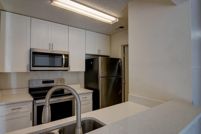 kitchen featuring white cabinetry, light stone countertops, stainless steel appliances, and a textured ceiling