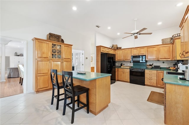 kitchen featuring ornate columns, a kitchen island, a kitchen breakfast bar, ceiling fan, and black appliances