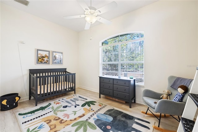 bedroom with ceiling fan, light hardwood / wood-style flooring, and a crib